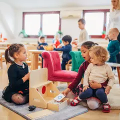 Dzieci na pasowaniu na przedszkolaka uczą się literek. Starsza dziewczynka pokazuje młodszemu dziecku kartę z literą "O".