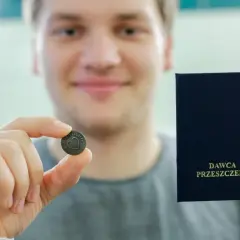 13 października. Młody mężczyzna trzyma medalik z sercem i kartę "DAWCA PRZESZCZEPU".