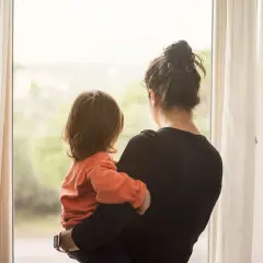 Samotna matka tuli swoje dziecko, patrząc przez okno na świat.
