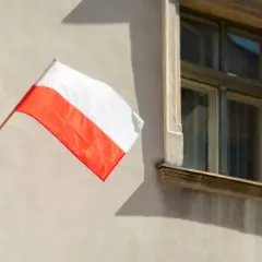 Biało-czerwona flaga Polski powiewa na tle jasnej ściany z oknami. Dziś 12 kwietnia, dzień dumy narodowej.