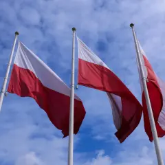 Trzy polskie flagi powiewają na wietrze na tle błękitnego nieba z chmurami. 16 sierpnia święto narodowe.