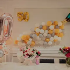 Pięćdziesiąte urodziny żony! Balony w kształcie cyfr 50, szampan i bukiety kwiatów tworzą radosną atmosferę.
