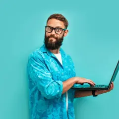 Zdziwiony mężczyzna z brodą i okularami, pracujący na laptopie. Dziś jest 13 września, a on wygląda, jakby odkrył coś zaskakującego.