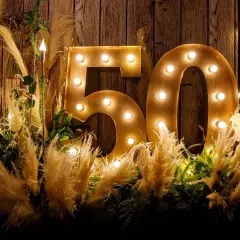 Złote litery "50" z żarówkami, otoczone puszystymi trawami i zielenią, tworzą magiczną dekorację na 50 urodziny.
