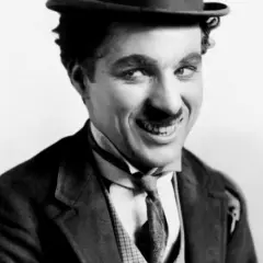 Charlie Chaplin w meloniku i garniturze, z uśmiechem, jakby opowiadał dowcip swoim dzieciom.