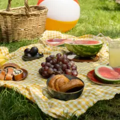 Piknik na trawie: koszyk, owoce (arbuz, winogrona, banany, śliwki), ciasto makowe, napoje i piłka plażowa. Idealny początek kalendarzowe lato 2026.