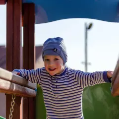 Uśmiechnięty chłopiec w czapce i pasiastym sweterku bawi się na placu zabaw. To pewnie jego imieniny Jakuba!