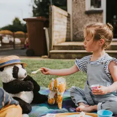Dziewczynka karmi pluszowego misia i słonika na trawie. Świetne pomysły na nudę w ogrodzie!