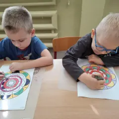 Dwóch chłopców z zapałem koloruje swoje mandale.