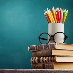 Stos książek, okulary i kolorowe kredki symbolizują drogę do wykształcenia i wiedzy.