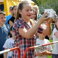 Dziewczynka trzyma pudełko na festynie rodzinnym, otoczona innymi dziećmi.