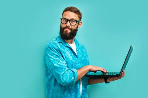Zdziwiony mężczyzna z brodą i okularami, pracujący na laptopie. Dziś jest 13 września, a on wygląda, jakby odkrył coś zaskakującego.