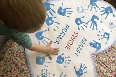 Dziecko tworzy kolaż z odcisków dłoni na sercu z napisem "Prawa swoje mamy".