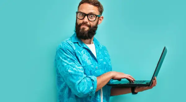 Zdziwiony mężczyzna z brodą i okularami, pracujący na laptopie. Dziś jest 13 września, a on wygląda, jakby odkrył coś zaskakującego.
