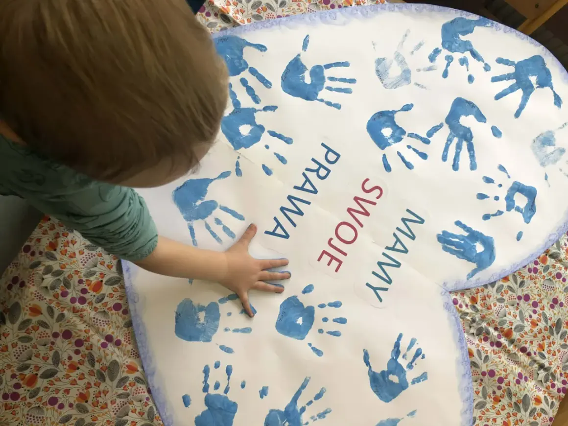 Dziecko tworzy kolaż z odcisków dłoni na sercu z napisem "Prawa swoje mamy".