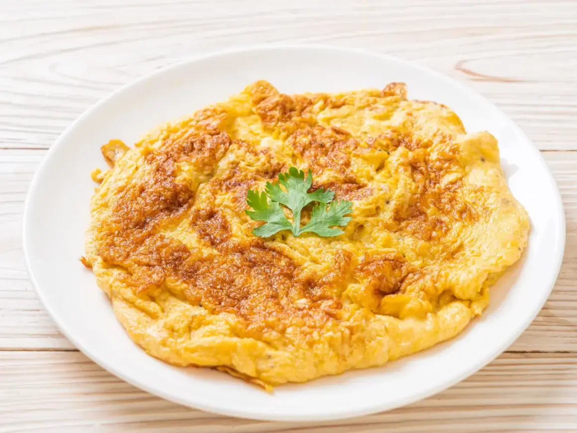Złocisty omlet na talerzu, idealny jako omlet dla niemowlaka. Delikatny, puszysty, z gałązką pietruszki.