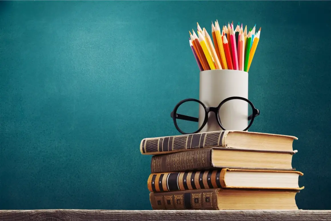 Stos książek, okulary i kolorowe kredki symbolizują drogę do wykształcenia i wiedzy.