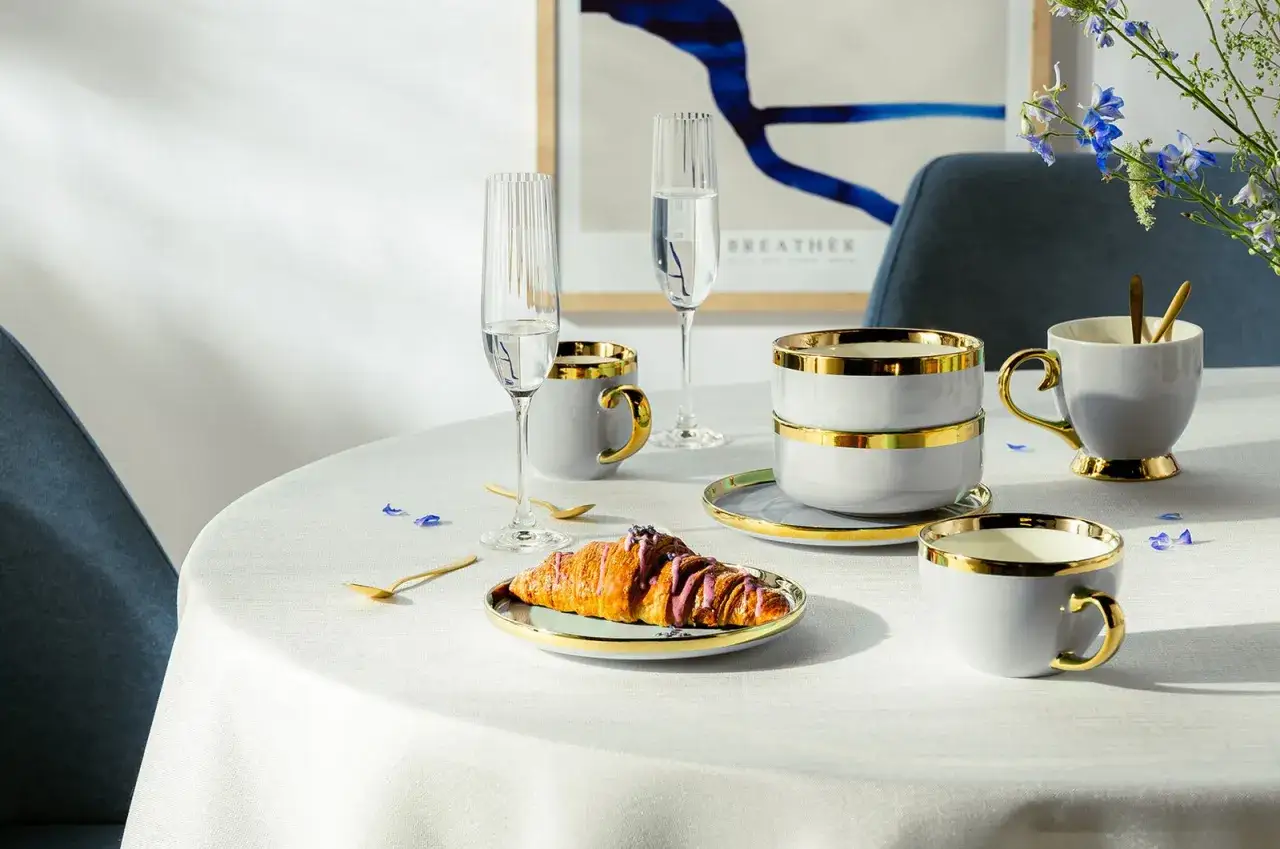 Elegancka porcelanowa zastawa z złotymi zdobieniami, kieliszki i rogalik na talerzyku – idealne na porcelanową rocznicę ślubu.