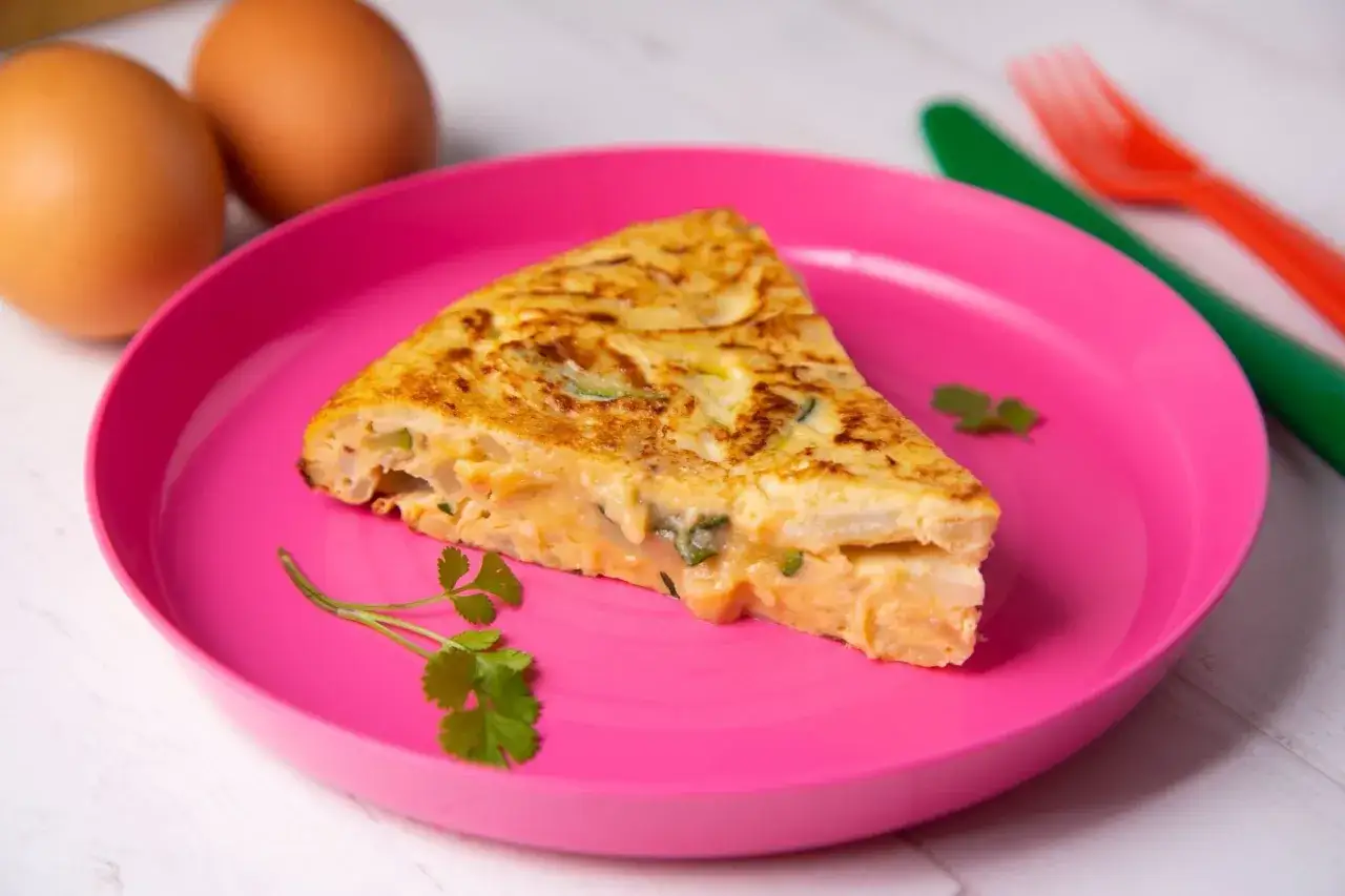 Pyszny omlet dla niemowlaka na różowym talerzyku, z jajkami i natką pietruszki w tle.