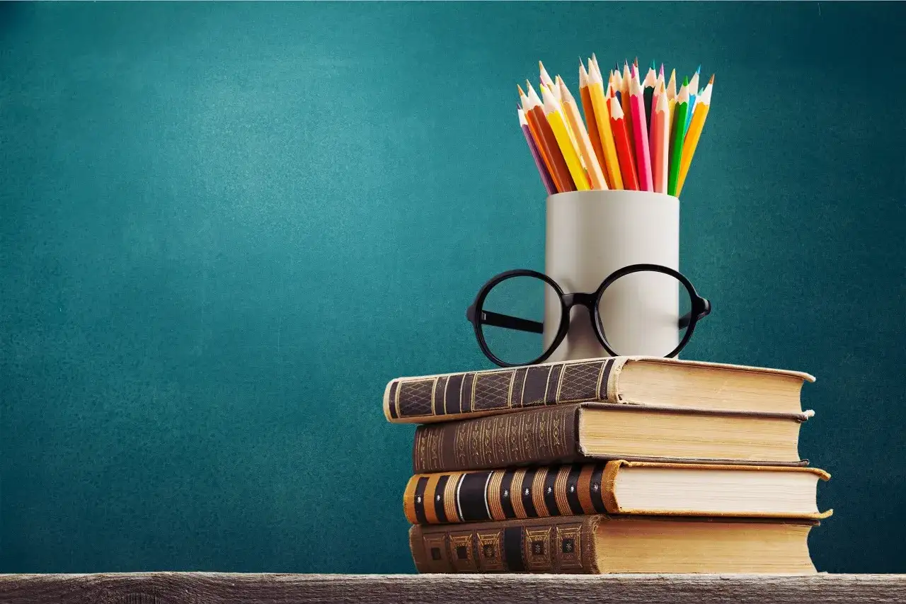 Stos książek, okulary i kolorowe kredki symbolizują drogę do wykształcenia i wiedzy.