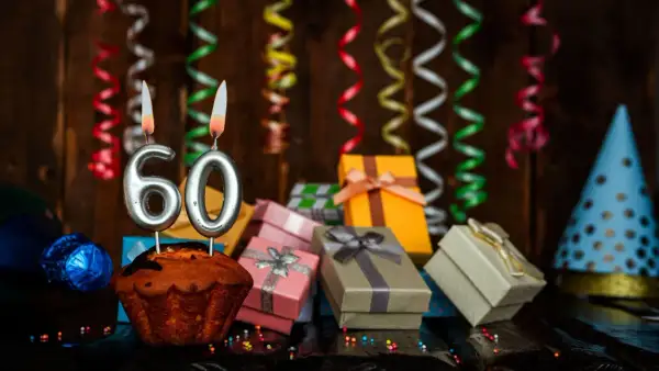 Uroczy tort z cyframi "60" i płonącymi świecami, otoczony prezentami i serpentynami. Idealne życzenia na 60 urodziny!