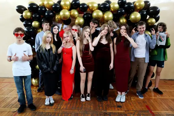 Uczniowie pozują do zdjęcia na tle balustrady z czarnych i złotych balonów. To ważny moment, być może zakończenie roku szkolnego lub studniówka.