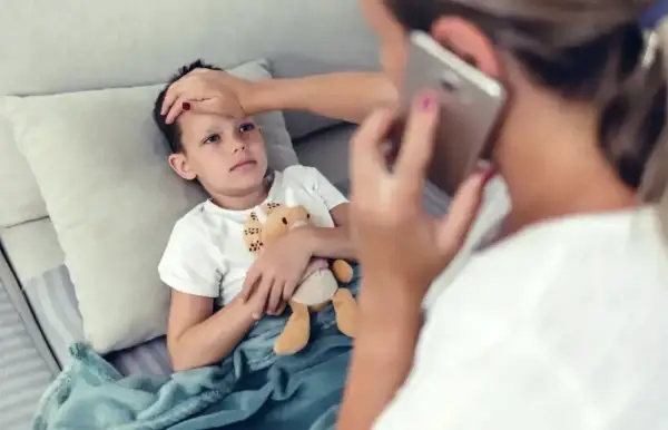 Chory chłopiec leży pod kocem, mama sprawdza mu temperaturę i dzwoni po pomoc. L4 na dziecko.