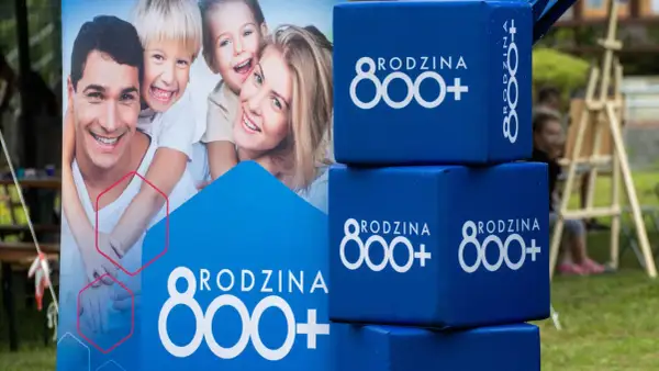 Uśmiechnięta rodzina na plakacie i niebieskie kostki z napisem "RODZINA 800+". Wniosek ZUS o świadczenie 800 plus to wsparcie dla rodzin.