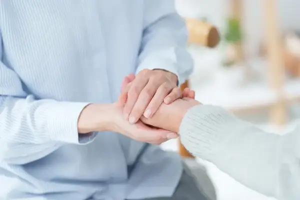 Dwie osoby trzymają się za ręce. Jedna osoba w niebieskiej koszuli, druga w białym swetrze. To świadczenie wspierające wyrównanie.
