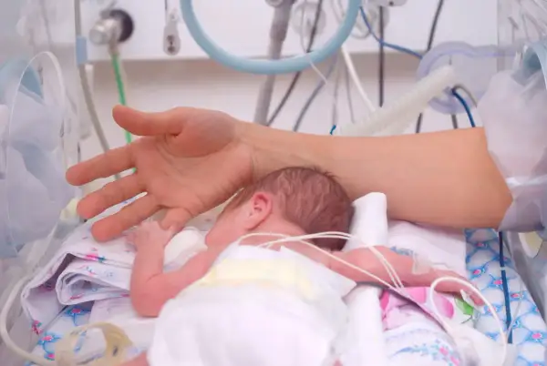 Dłoń matki czule dotyka noworodka w inkubatorze. To obraz nadziei i miłości, który może być częścią wniosku o urlop macierzyński.