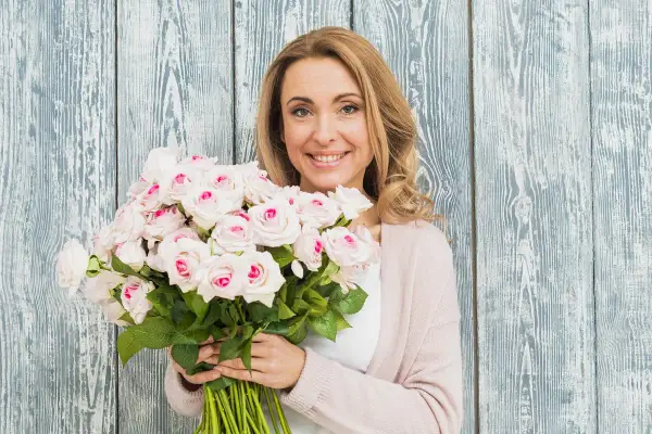 Uśmiechnięta blondynka z bukietem jasnoróżowych róż, gotowa na imieniny Jana.