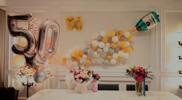 Pięćdziesiąte urodziny żony! Balony w kształcie cyfr 50, szampan i bukiety kwiatów tworzą radosną atmosferę.