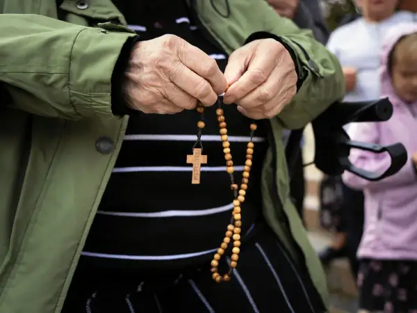 Dłoń starszej osoby trzyma paciorki różańca, odmawiając modlitwę do anioła stróża za dorosłe dzieci.