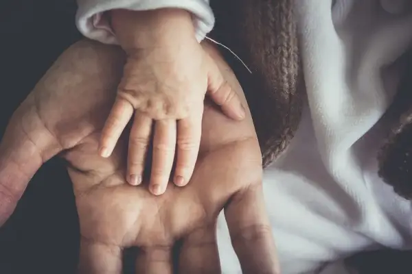 Dłoń dorosłego obejmuje dłoń niemowlęcia. To symbol opieki nad zdrowym dzieckiem, czułości i bezpieczeństwa.