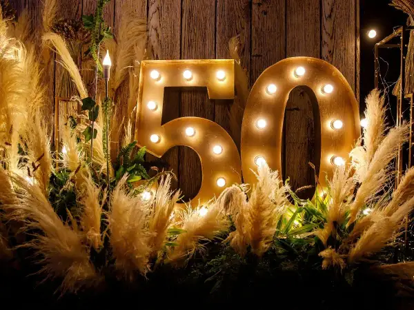 Złote litery "50" z żarówkami, otoczone puszystymi trawami i zielenią, tworzą magiczną dekorację na 50 urodziny.