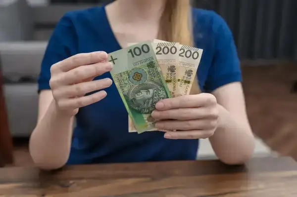 Dłonie trzymają banknoty 100 i 200 zł. Zastanawiasz się, kosiniakowe dla kogo? To pieniądze na wyprawkę dla dziecka.