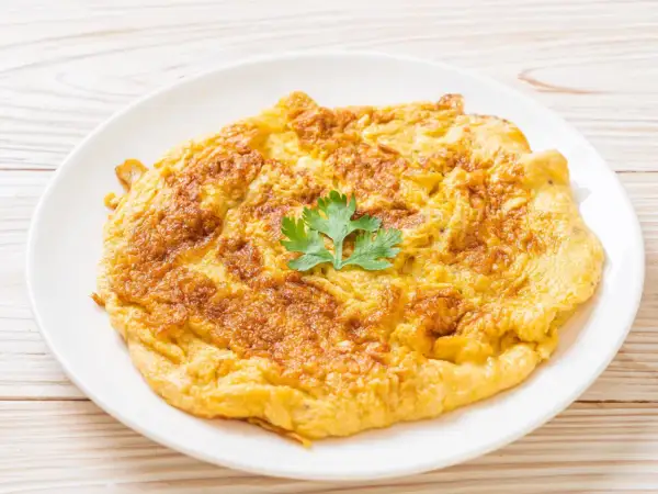 Złocisty omlet na talerzu, idealny jako omlet dla niemowlaka. Delikatny, puszysty, z gałązką pietruszki.